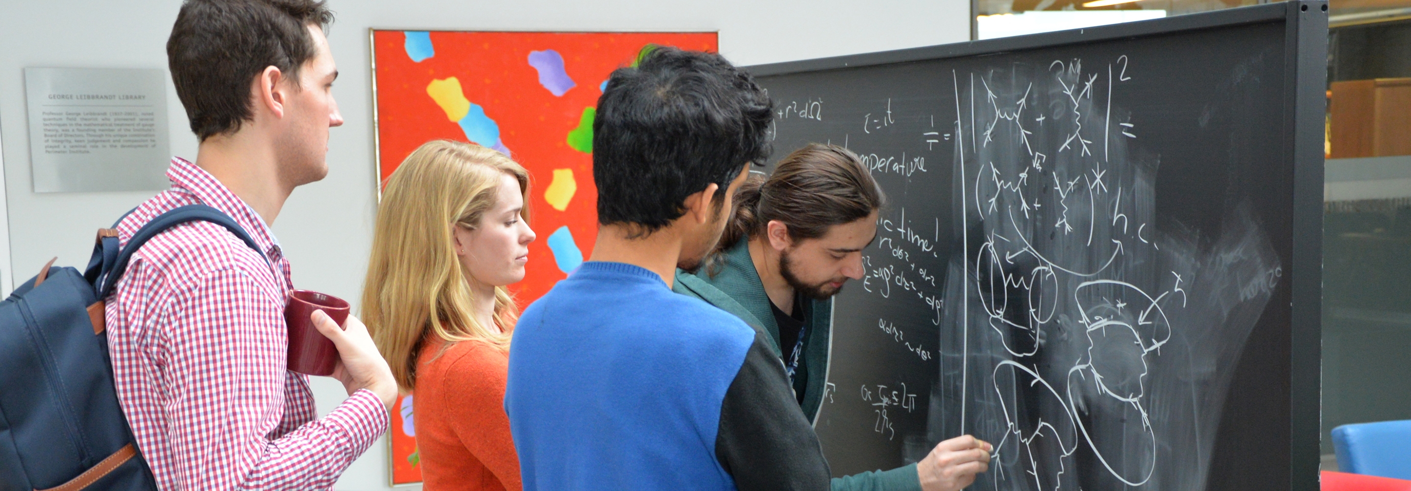 Three men and a woman standing at a chalkboard working on equations