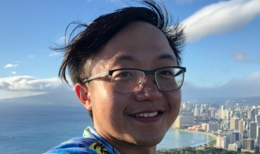 Young man with glasses with city and ocean view behind him