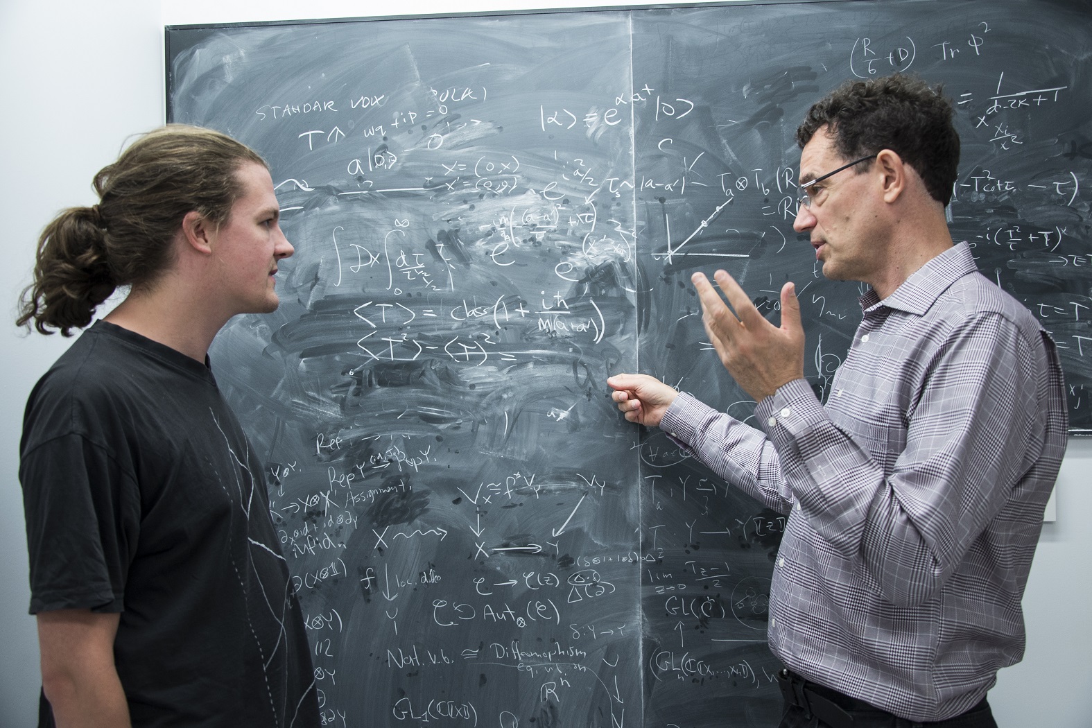 Steffen Gielen and Neil Turok interacting in front of a blackboard covered in equations and graphs