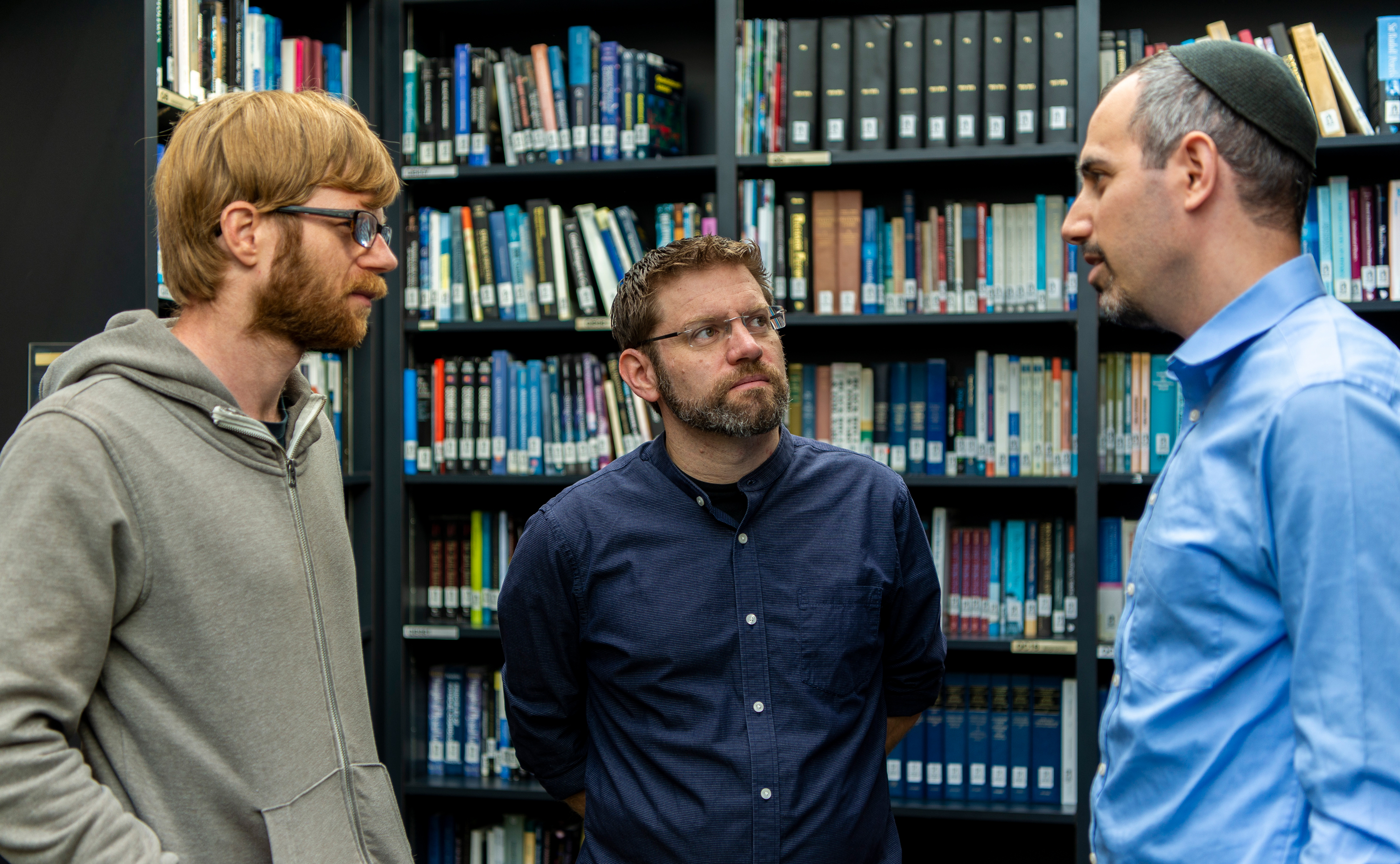 Three men standing in a library having a conversation together