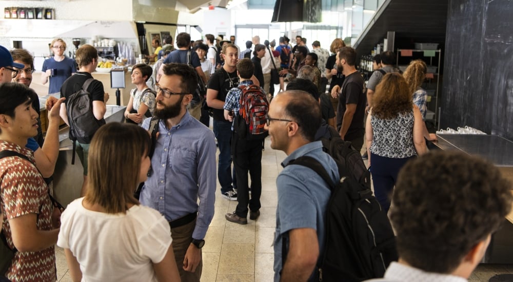 Crowd of people talking in groups in a building hallway