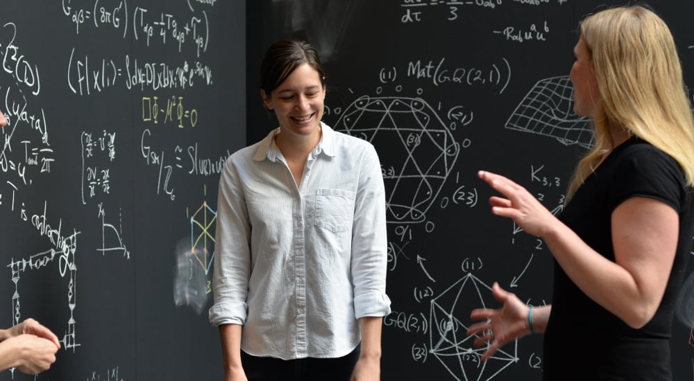 Three women surrounded by chalkboards with equations