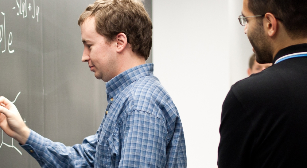 Man standing at blackboard teaching to 3 other men