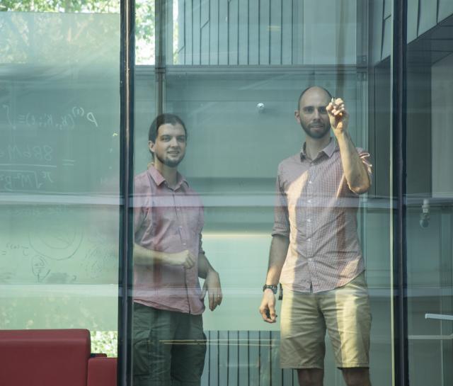 Two men writing equations on a glass wall