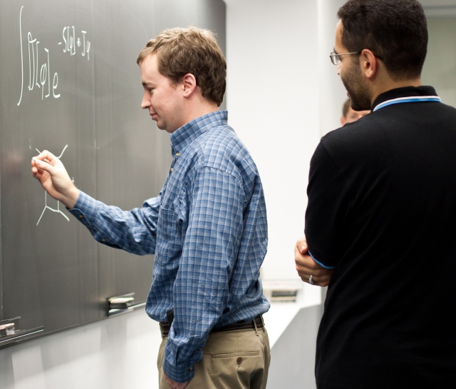 Man writing on the chalkboard with other men standing behind him