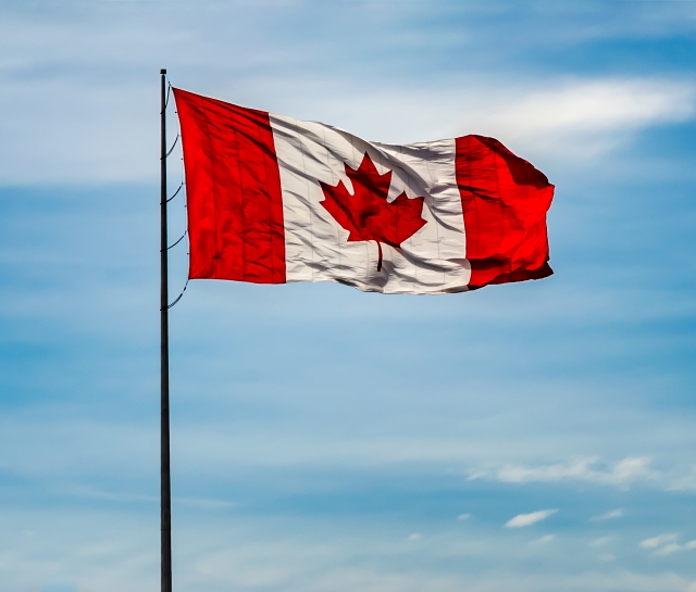 Canada flag flying with a blue cloudy sky behind it