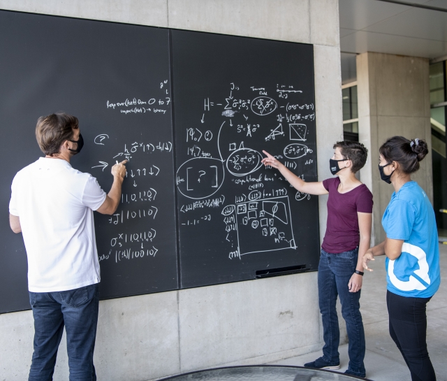 Man and two women working together on a blackboard outside