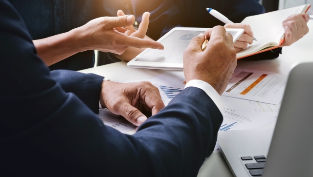 Close up of men and women's hands going over paperwork and a tablet of information