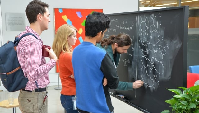 group of PSI students working together on a blackboard in the atrium at Perimeter Institute