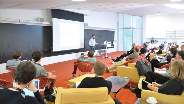 Man standing at the front of a lecture hall talking to people