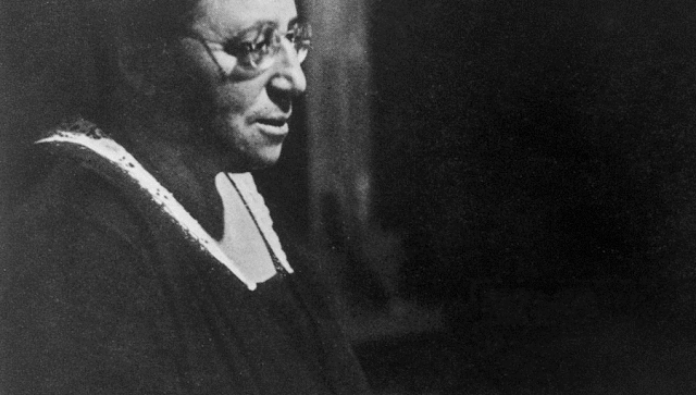 Black and white photo of a woman with glasses in a black cloak