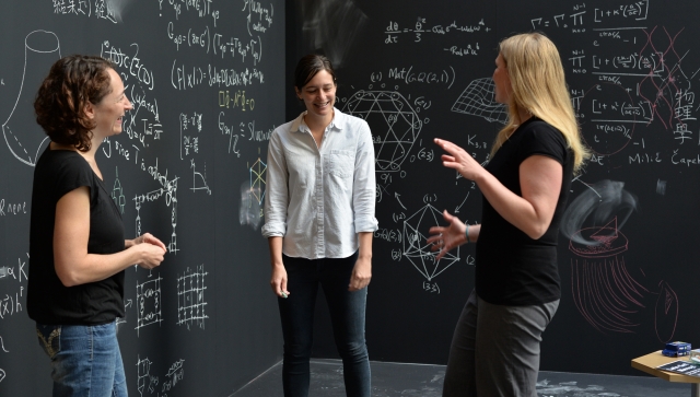 Three women surrounded by chalkboards with equations