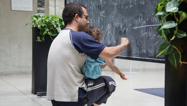 Man holding baby and writing equations on a blackboard