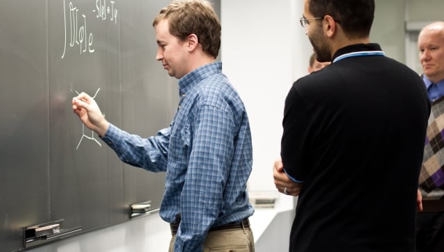 Man writing on the chalkboard with other men standing behind him