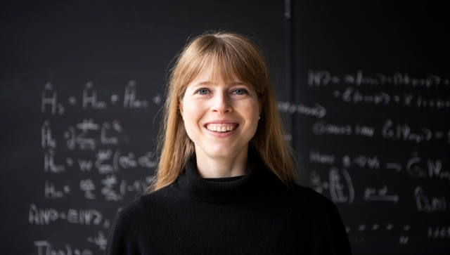Portrait of Christine Muschik in front of a blackboard of equations