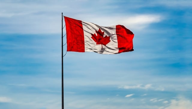 Canada flag flying with a blue cloudy sky behind it