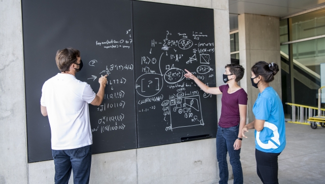 Man and two women working together on a blackboard outside