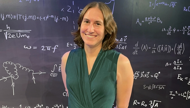 Woman wearing a green shirt standing in front of a blackboard of equations