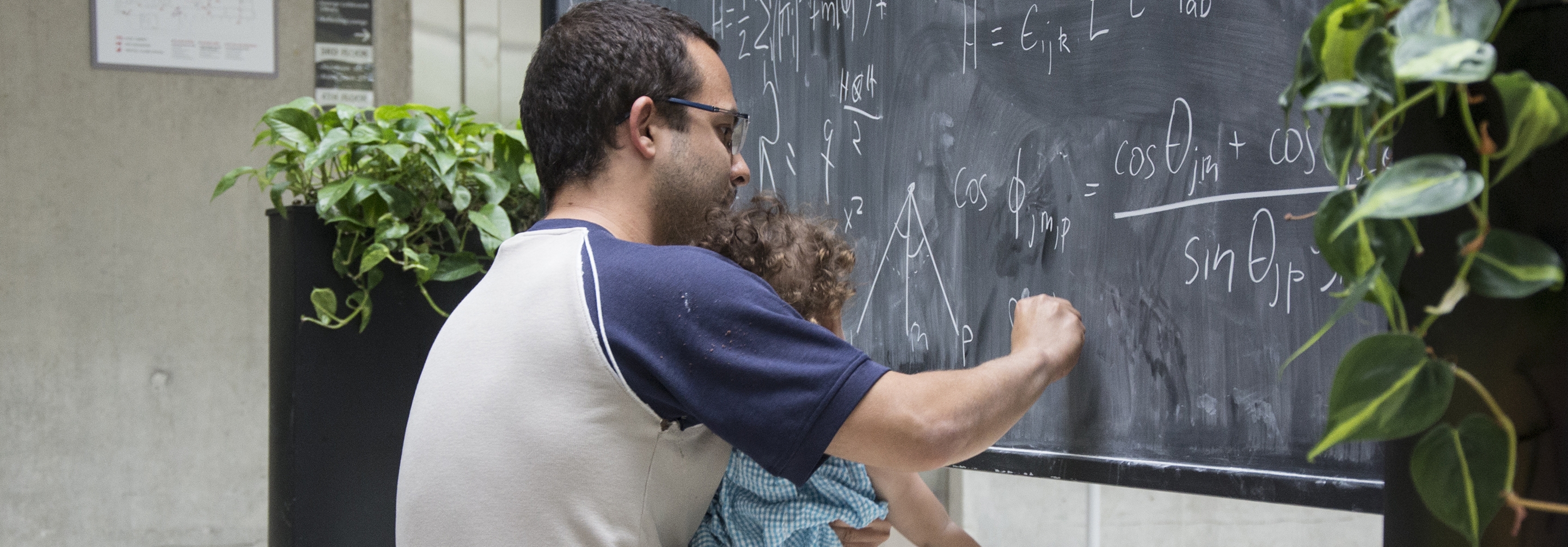 Man holding baby and writing equations on a blackboard