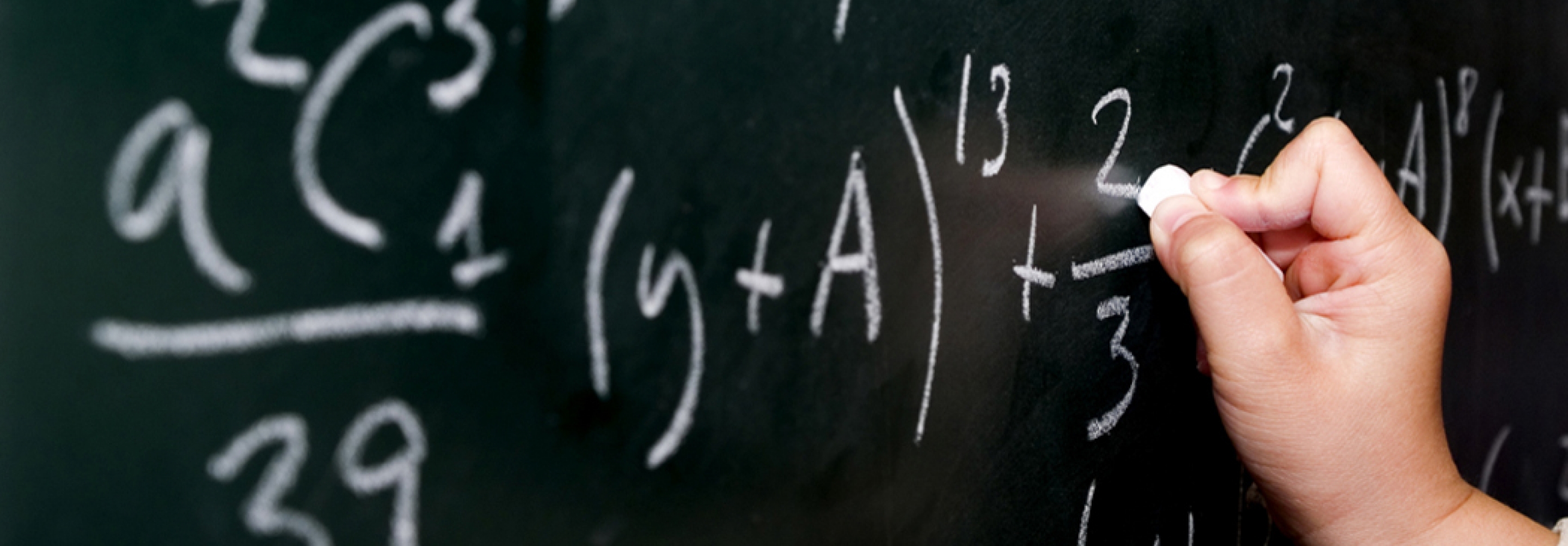 Picture of a hand writing equations on a blackboard