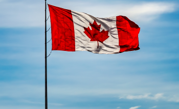 Canadian flag floating in the air against blue sky