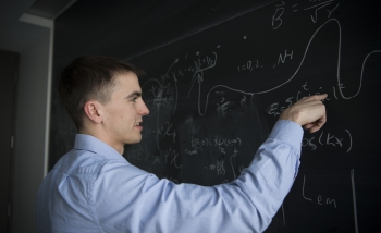Man in a blue collared shirt working with equations on a blackboard