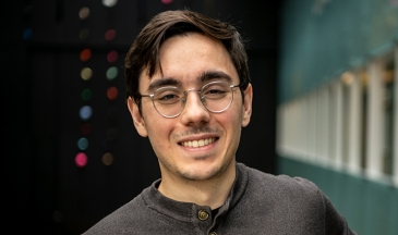 Portrait of a young man wearing glasses and a brown shirt in an atrium