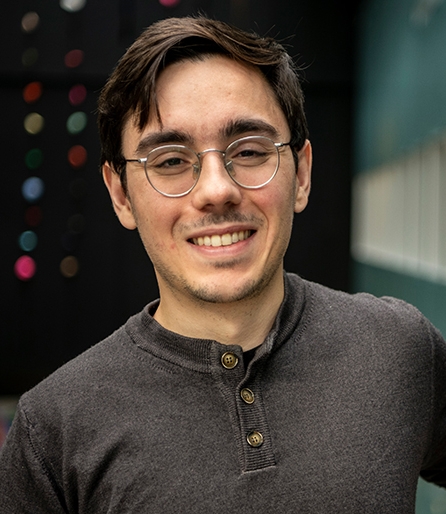 Portrait of a young man wearing glasses and a brown shirt in an atrium